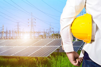 Midsection of engineer with hardhat standing against solar panel