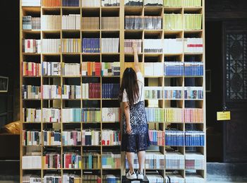 Full length rear view of girl standing in shelf