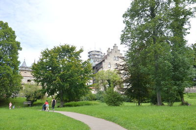 People walking on grass by trees against sky