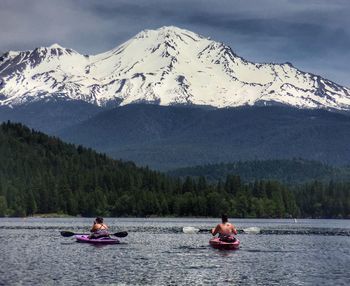 People in kayak on lake against snowcapped mountains