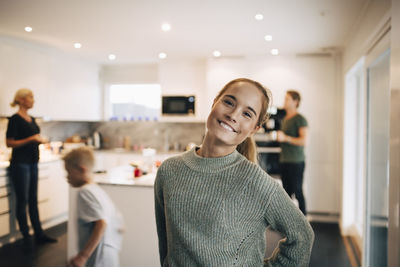 Portrait of smiling teenage girl standing against family in kitchen