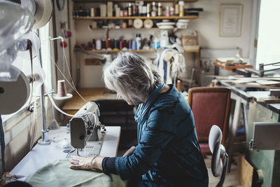 Senior female owner using sewing machine at workshop