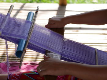 Cropped hands of woman weaving thread in loom