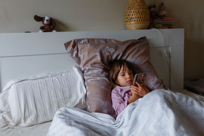 Sick child laying in the bed watching cellphone