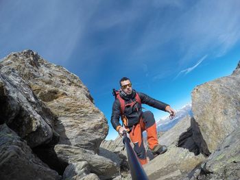 Full length of hiker taking selfie while standing on rock against blue sky