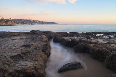 Rocky shore and sea against sky during sunset 