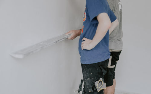 Two caucasian plasterer man checks the evenness of the walls after puttying.