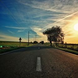 Street amidst field against sky during sunset