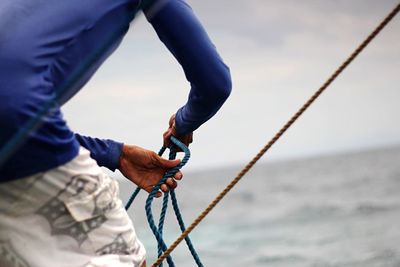 Low section of man holding rope against sea