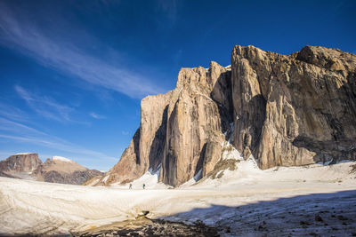 Distant view of mountaineers hiking under large mountain.