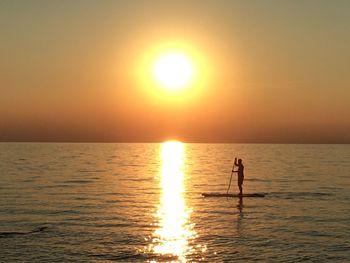 Silhouette person standing in sea against sky during sunset