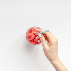 Close-up of hand holding strawberry over white background