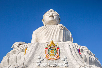 Low angle view of giant buddha statue against clear blue sky