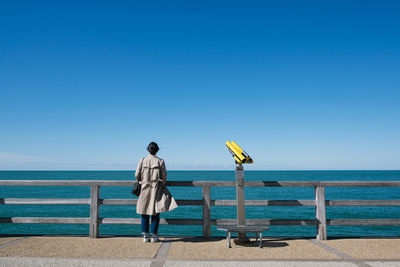 Rear view of man standing at beach against clear blue sky