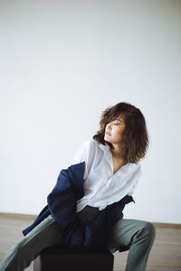 Side view of young woman sitting against wall