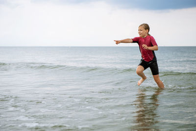 Full length of playful girl pointing in sea against sky