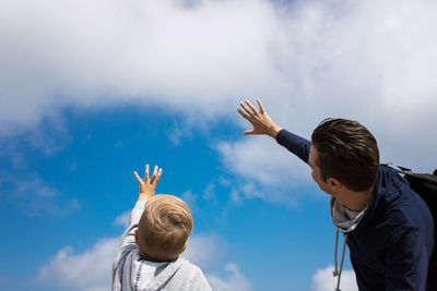 Rear view of friends with arms raised against sky