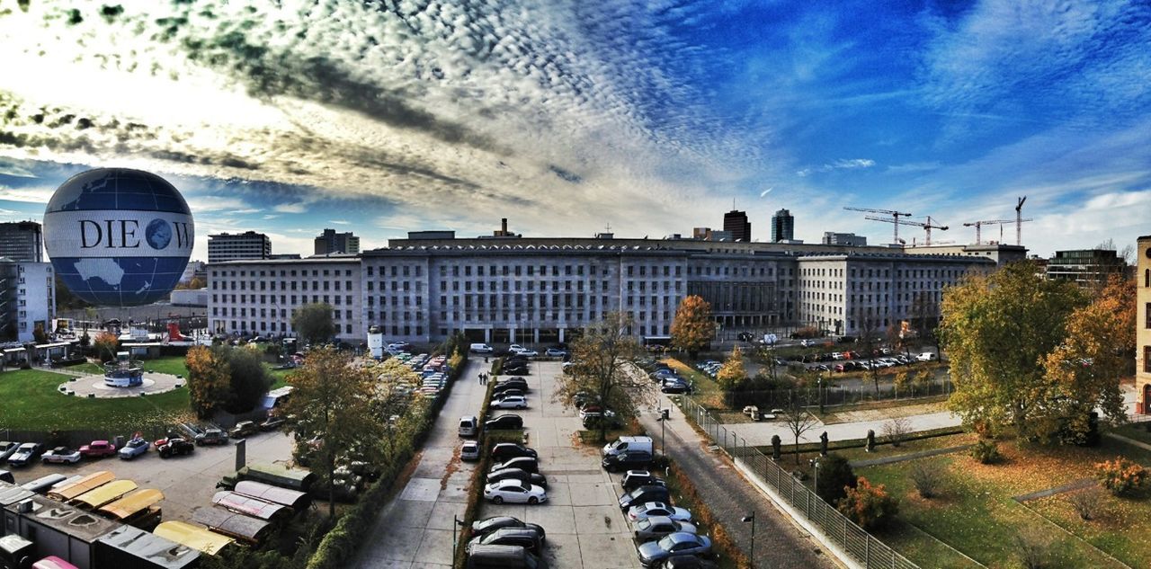 transportation, sky, car, building exterior, land vehicle, architecture, road, built structure, cloud - sky, city, street, mode of transport, high angle view, road marking, cloud, cloudy, city life, travel, day, cityscape