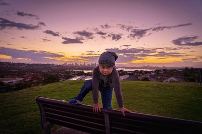 Portrait of boy climbing on bench during sunset