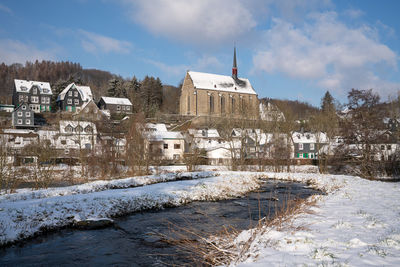 Snow covered houses by buildings against sky