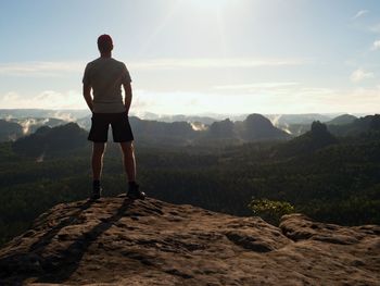 Young hiker in black pants and shirt on cliff edge and looking to misty hilly valley. hike man.