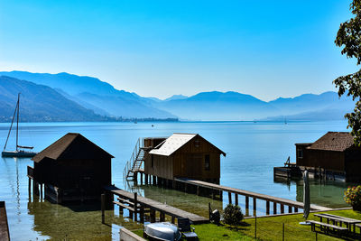 Houses by lake and mountains against blue sky