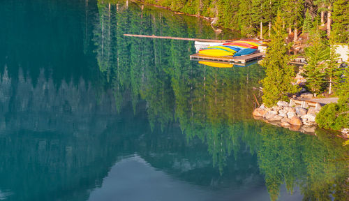 Canoes on jetty in lake with trees reflection