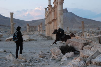 Man watching friend riding horse at old ruins