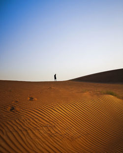 Distant view of woman standing at desert against sky during sunset