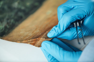 Female conservator with magnifying goggles cleaning dirt from antique oil painting