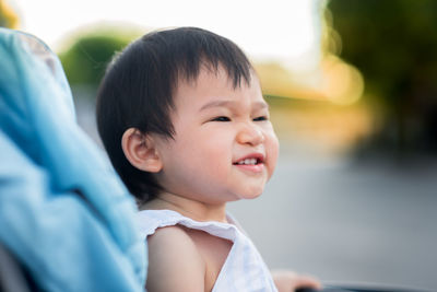Smiling baby looking away while sitting in carriage outdoors