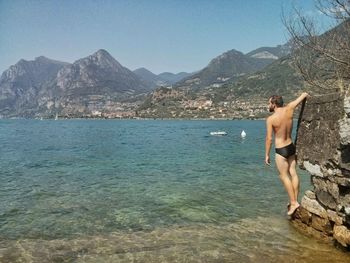 Midsection of shirtless man in sea against mountains