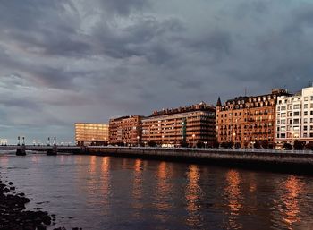 Buildings by river against sky in city at dusk