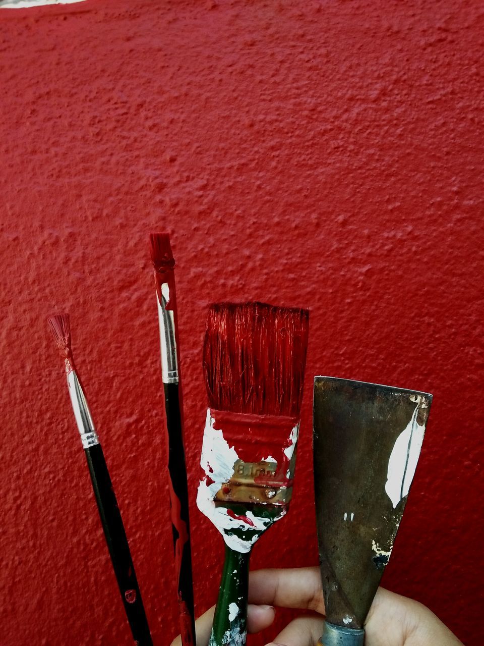 red, brush, paintbrush, holding, indoors, human hand, wall - building feature, one person, hand, close-up, real people, human body part, paint, high angle view, unrecognizable person, leisure activity, art and craft equipment, choice, still life, finger, home improvement