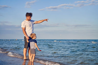 Father with son standing at beach against sky