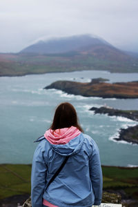 Rear view of woman in blue jacket looking at sea against sky