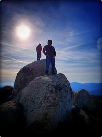 Rear view of men standing on rock against sky