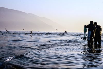 People standing in sea against clear sky