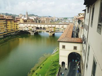 Arch bridge over river amidst buildings in city against sky