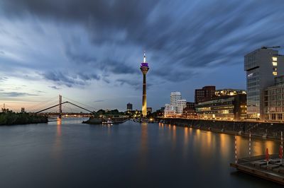 Illuminated buildings by river against sky in city