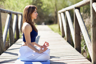 Side view of beautiful mid adult woman doing yoga on boardwalk