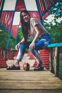 Full length of happy woman sitting on wood