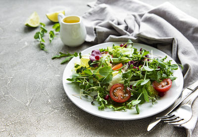 Fresh green mixed salad bowl with tomatoes and microgreens on concrete background. 