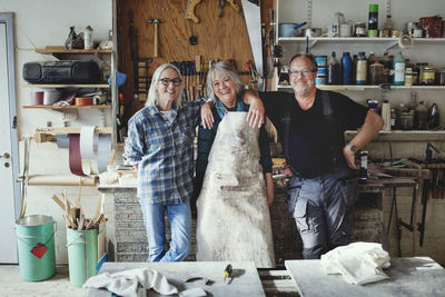 Portrait of cheerful senior coworkers standing against tools at workshop