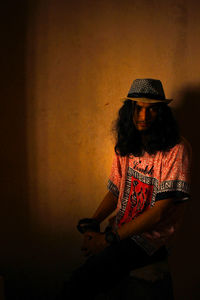 Woman wearing hat sitting against wall