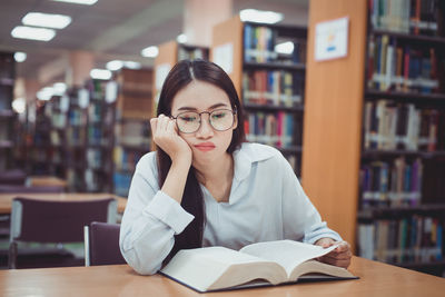Young woman reading book at table in library
