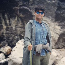 Portrait of young man in sunglasses standing against mountain