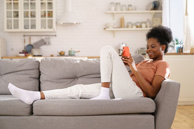 Smiling woman using mobile phone while sitting on sofa at home