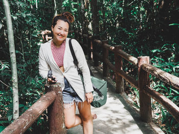 Young woman using mobile phone while sitting on tree in forest