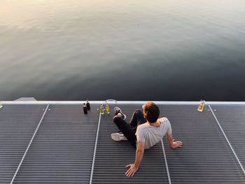 Rear view of man sitting on pier over lake